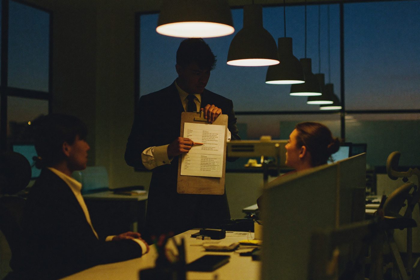 A team lead talks two specialists through the start of a shift at their desks in a quiet office at dusk
