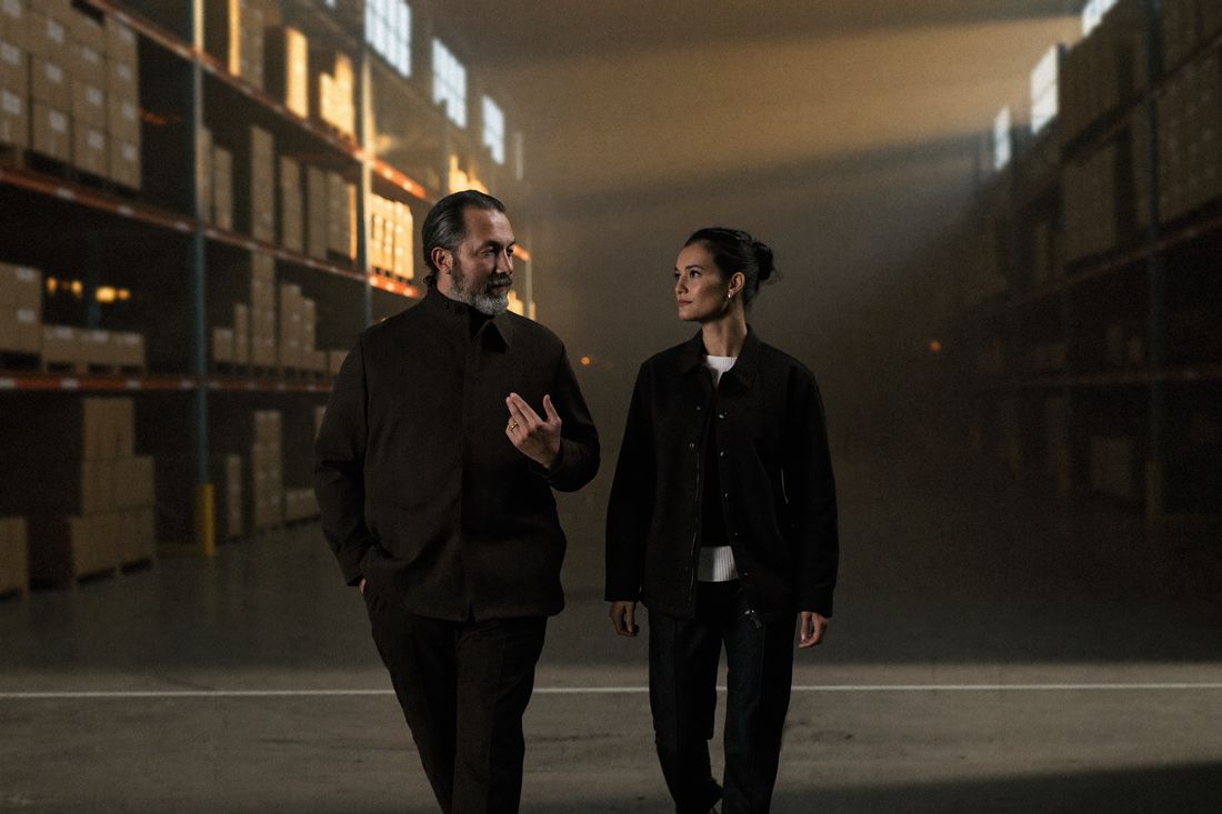 An experienced mentor talks with a trainee as they walk down a wide logistics warehouse aisle