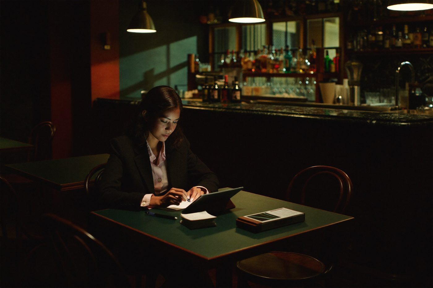 A restaurant owner reviews the day on a tablet at a corner table of her empty dining room after closing